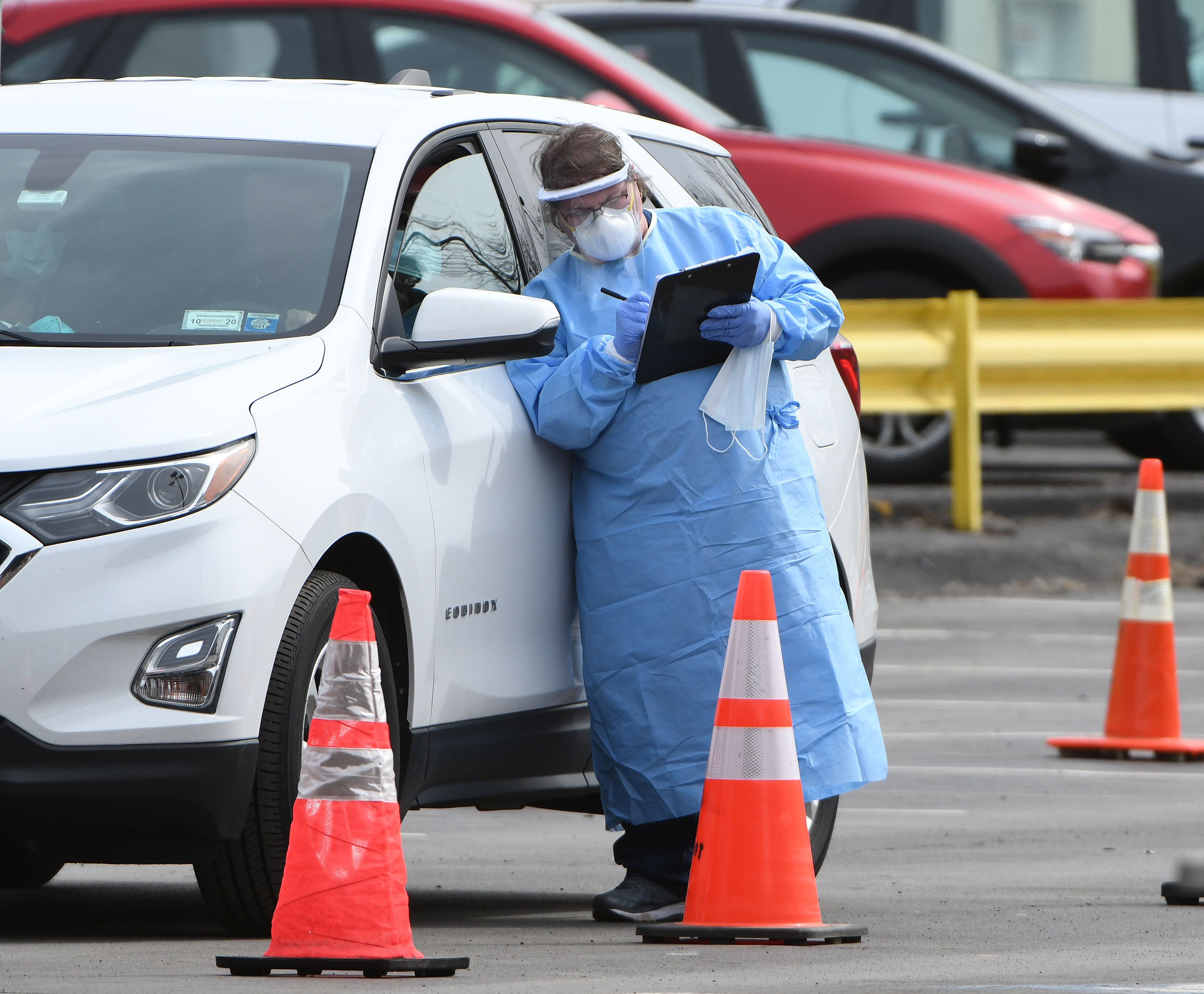 A medical worker in protective gear speaks with a patient in a car